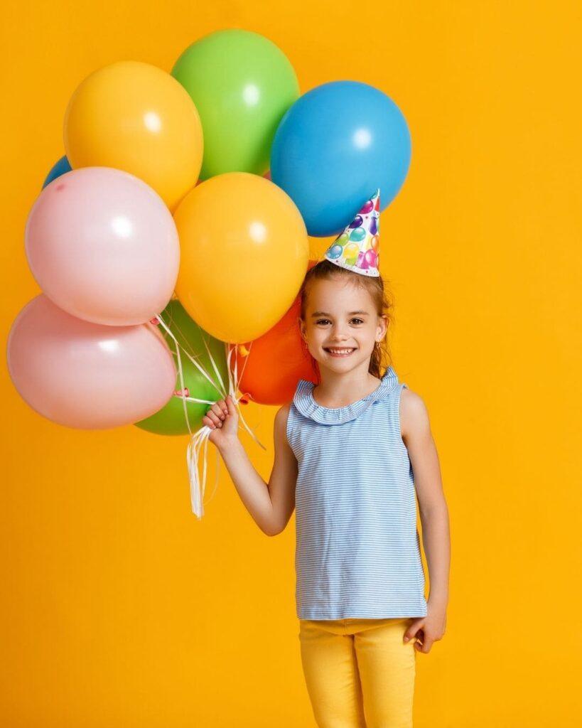 Menina segurando balões com fundo amarelo